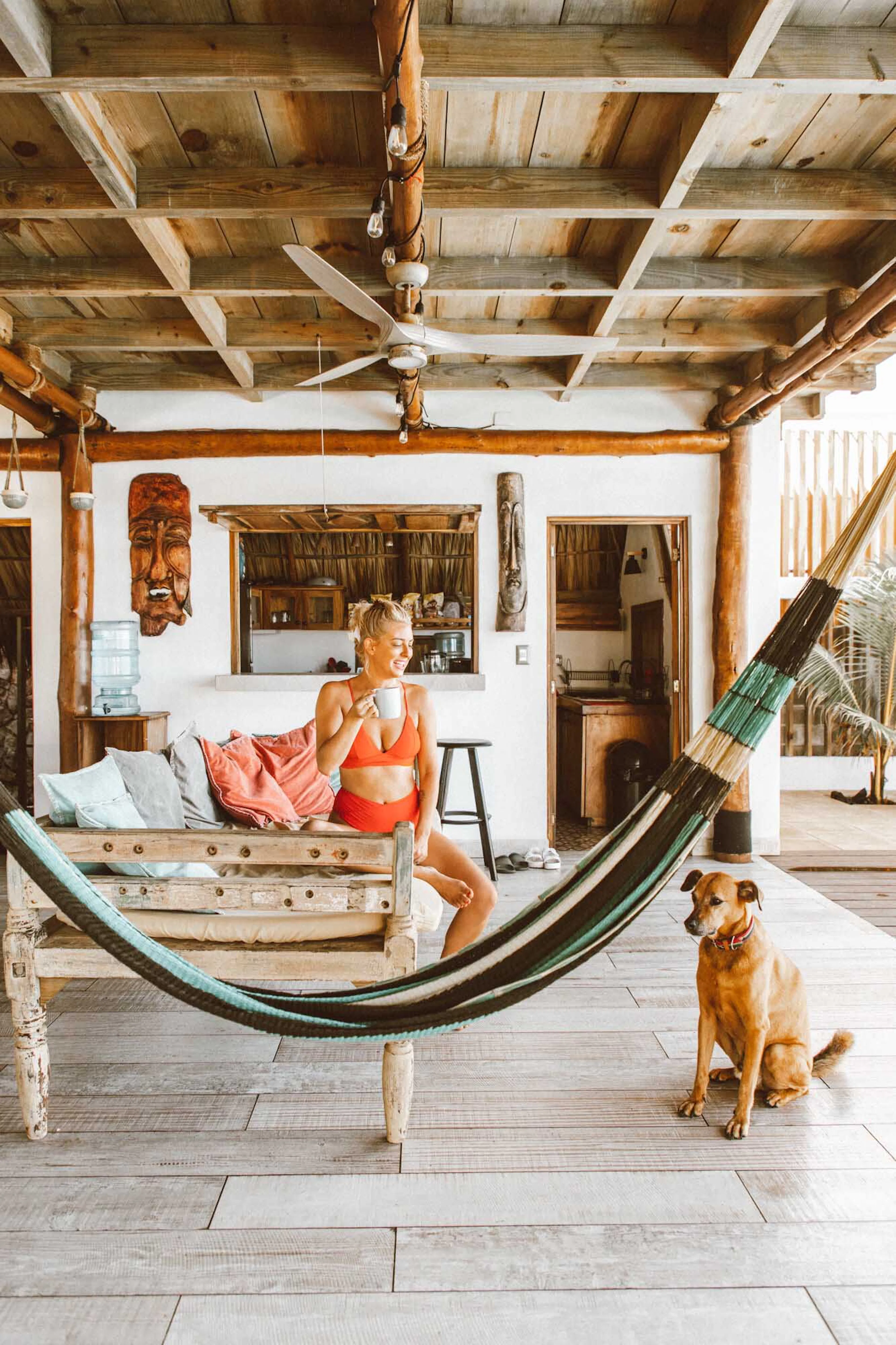 A woman relaxing on an open-air porch beside a hammock and a dog