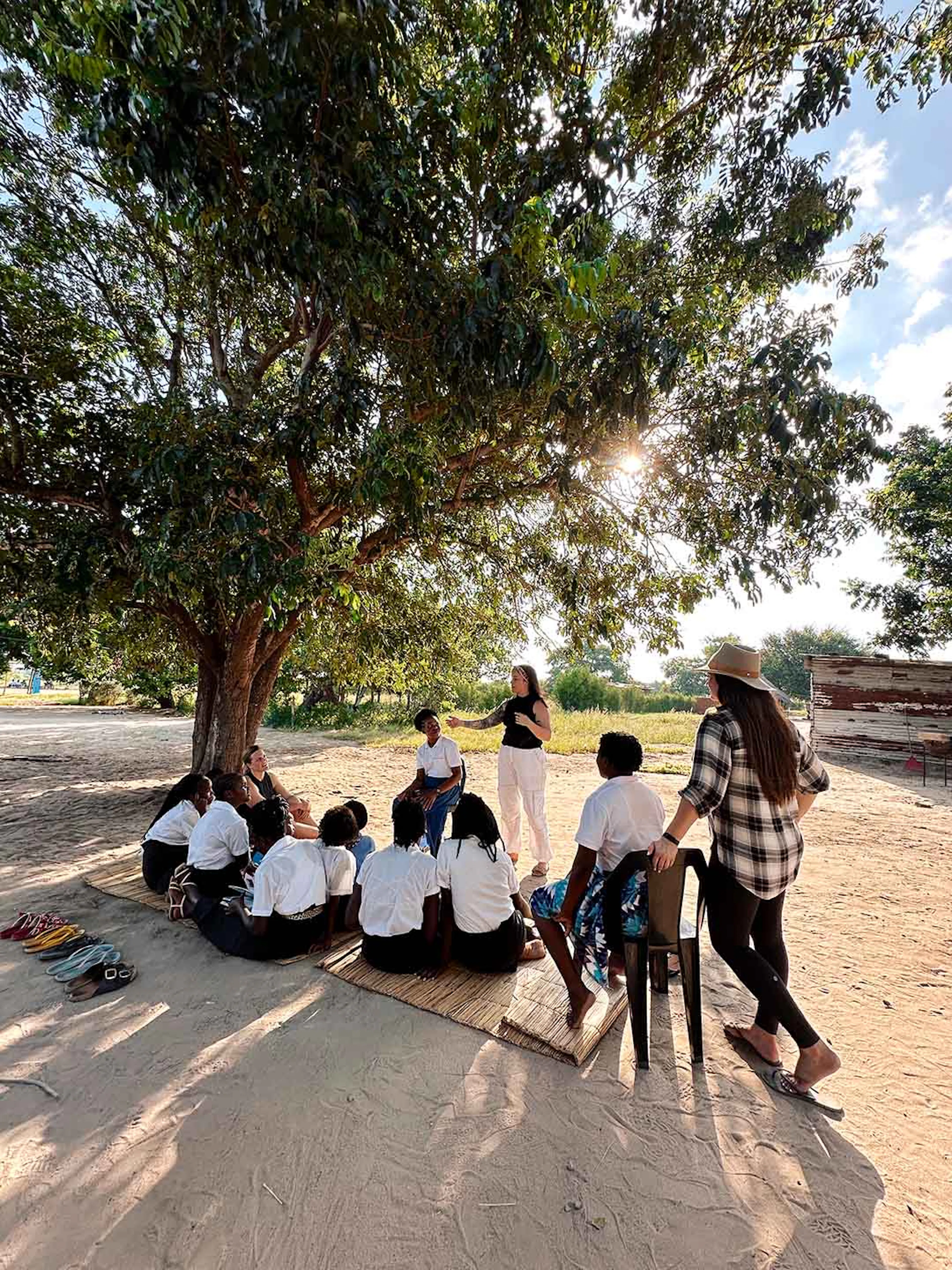A group sitting on mats in the shade of a large tree