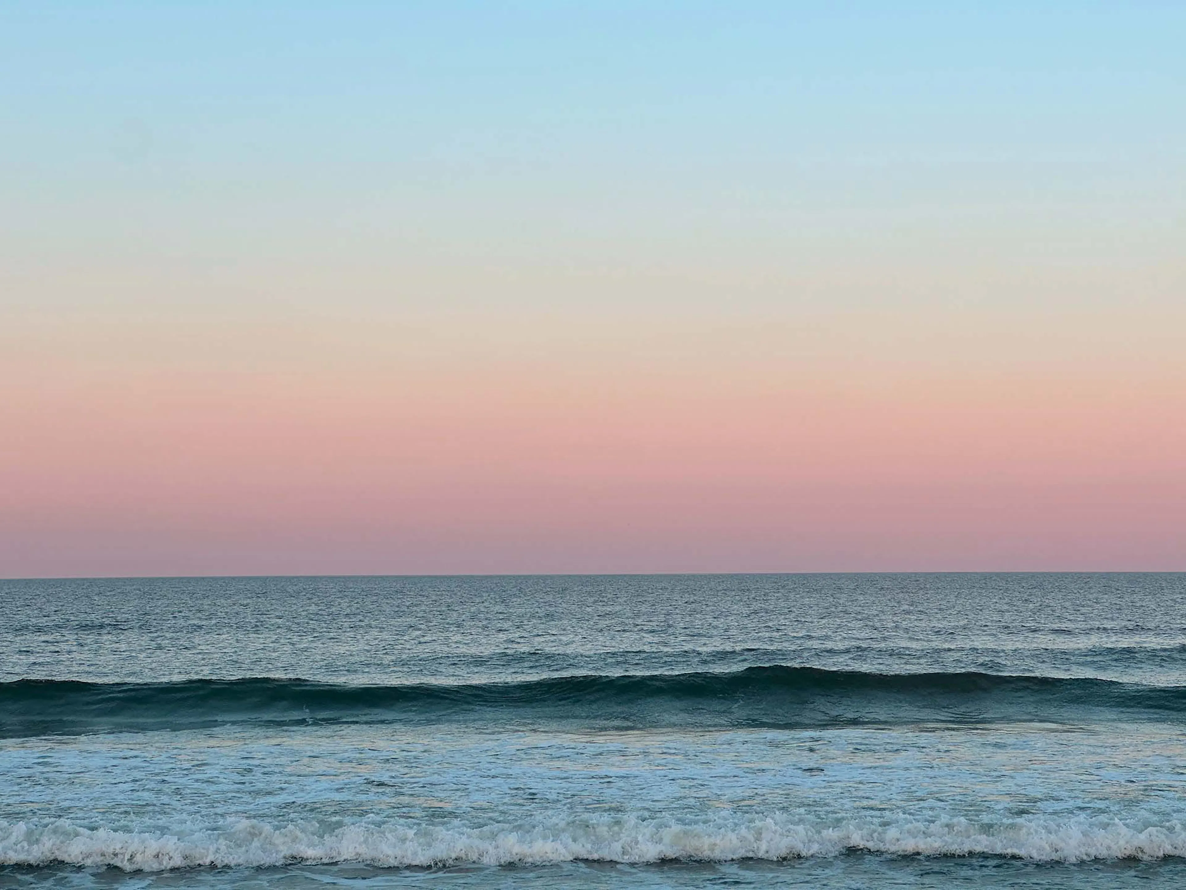 The ocean at sunset under a pink sky
