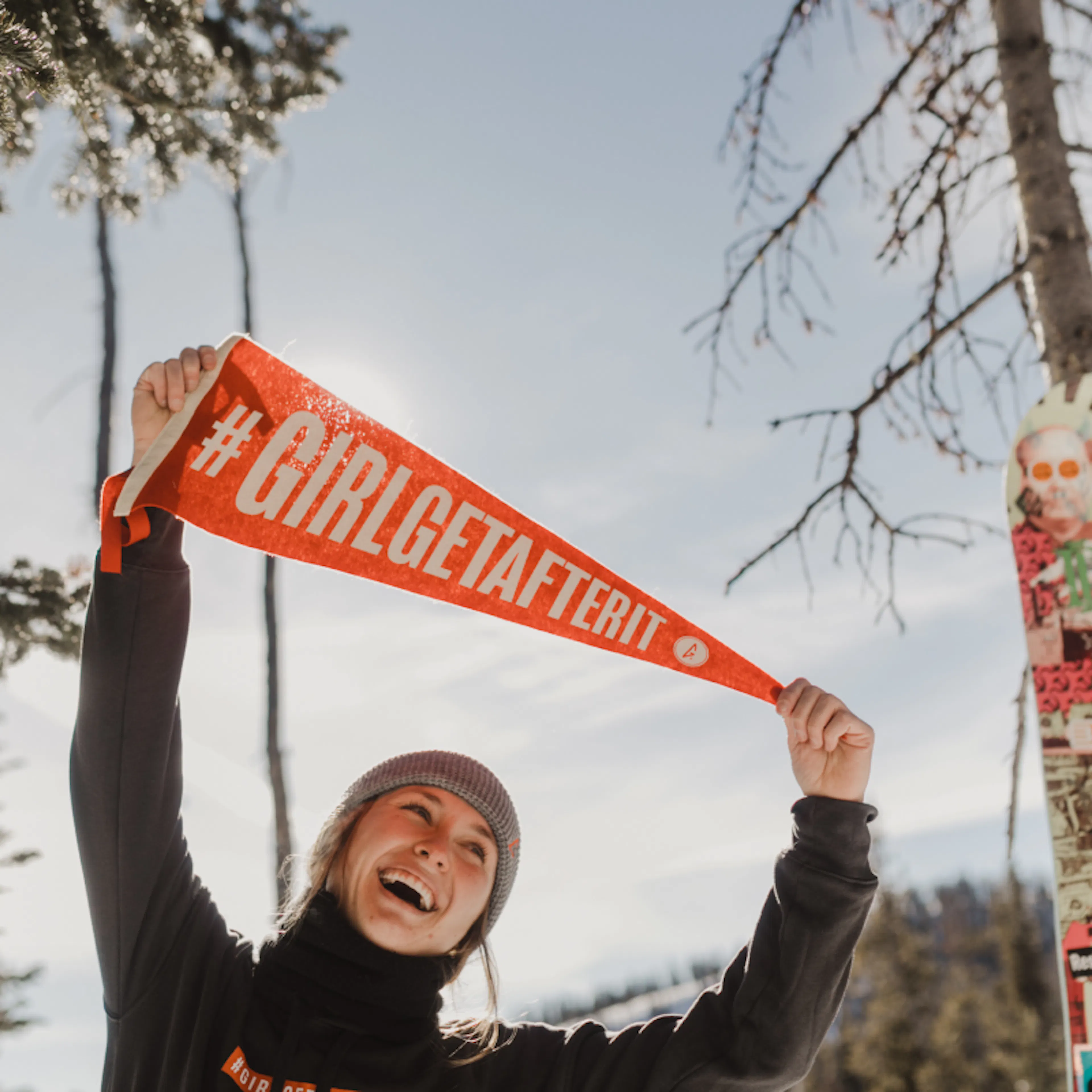 A woman holding up an orange #GirlGetAfterIt pennant
