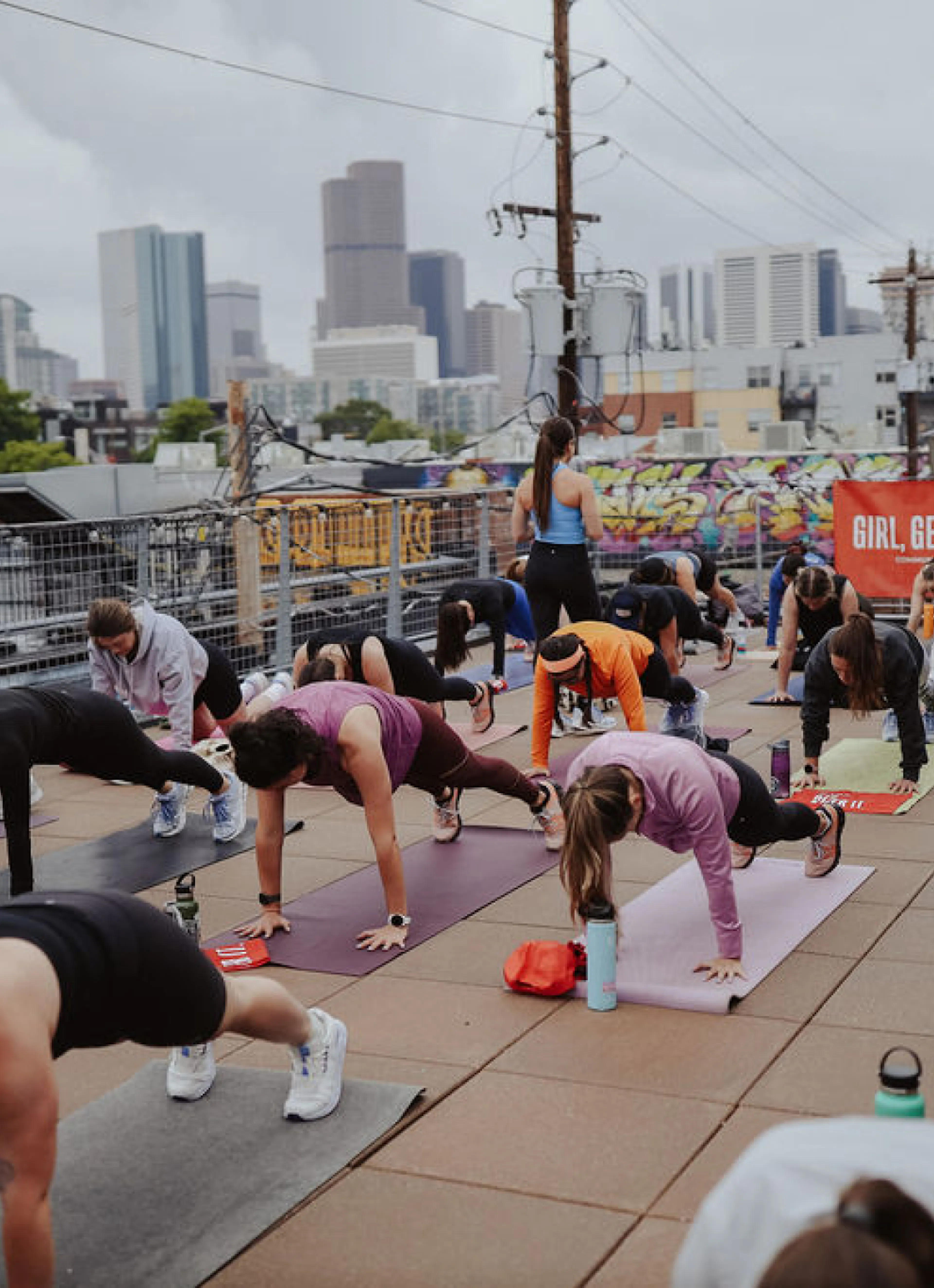 Women holding planks during a rooftop workout with a city skyline behind