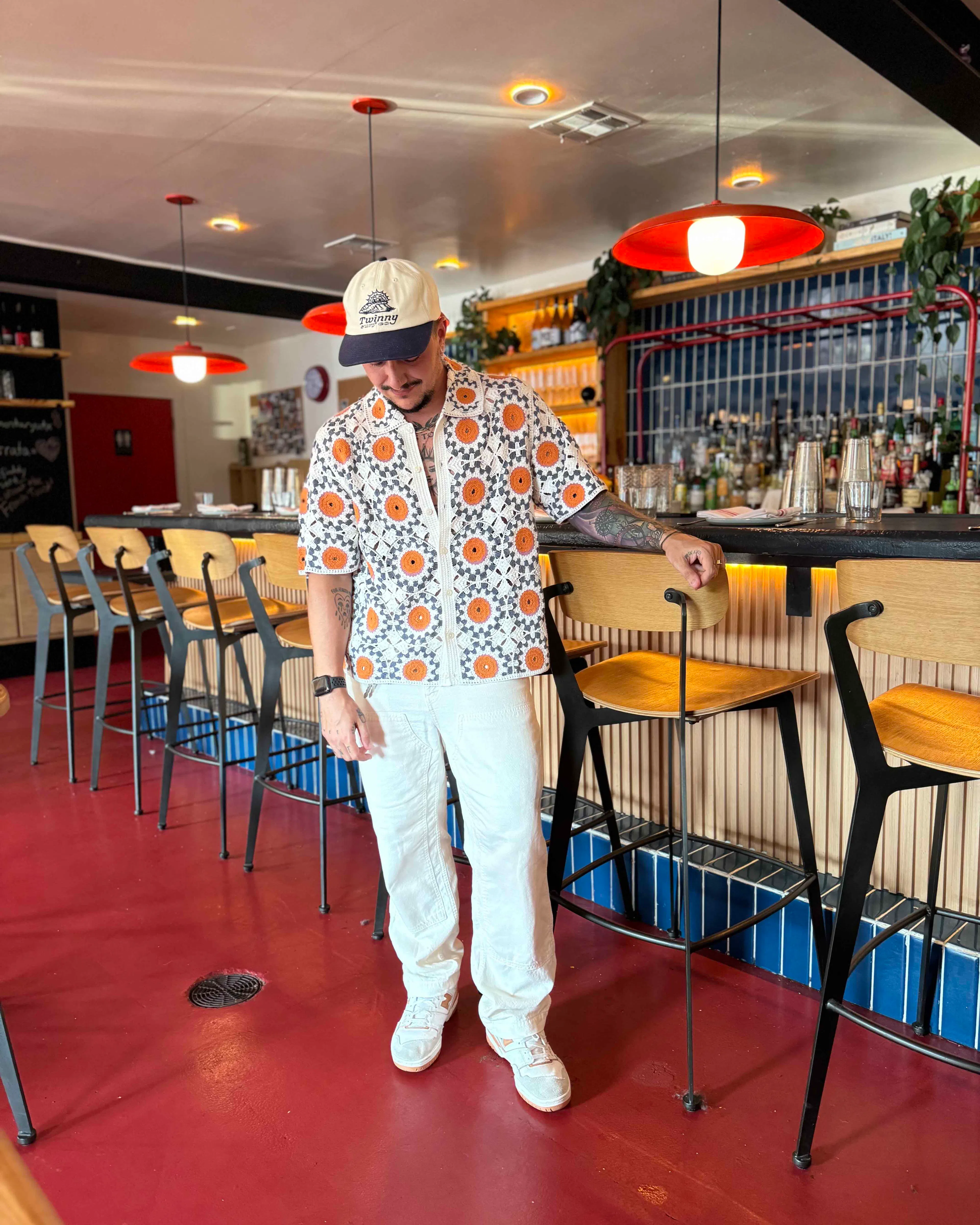 Chris Rhodes in a patterned shirt and white pants inside a bar