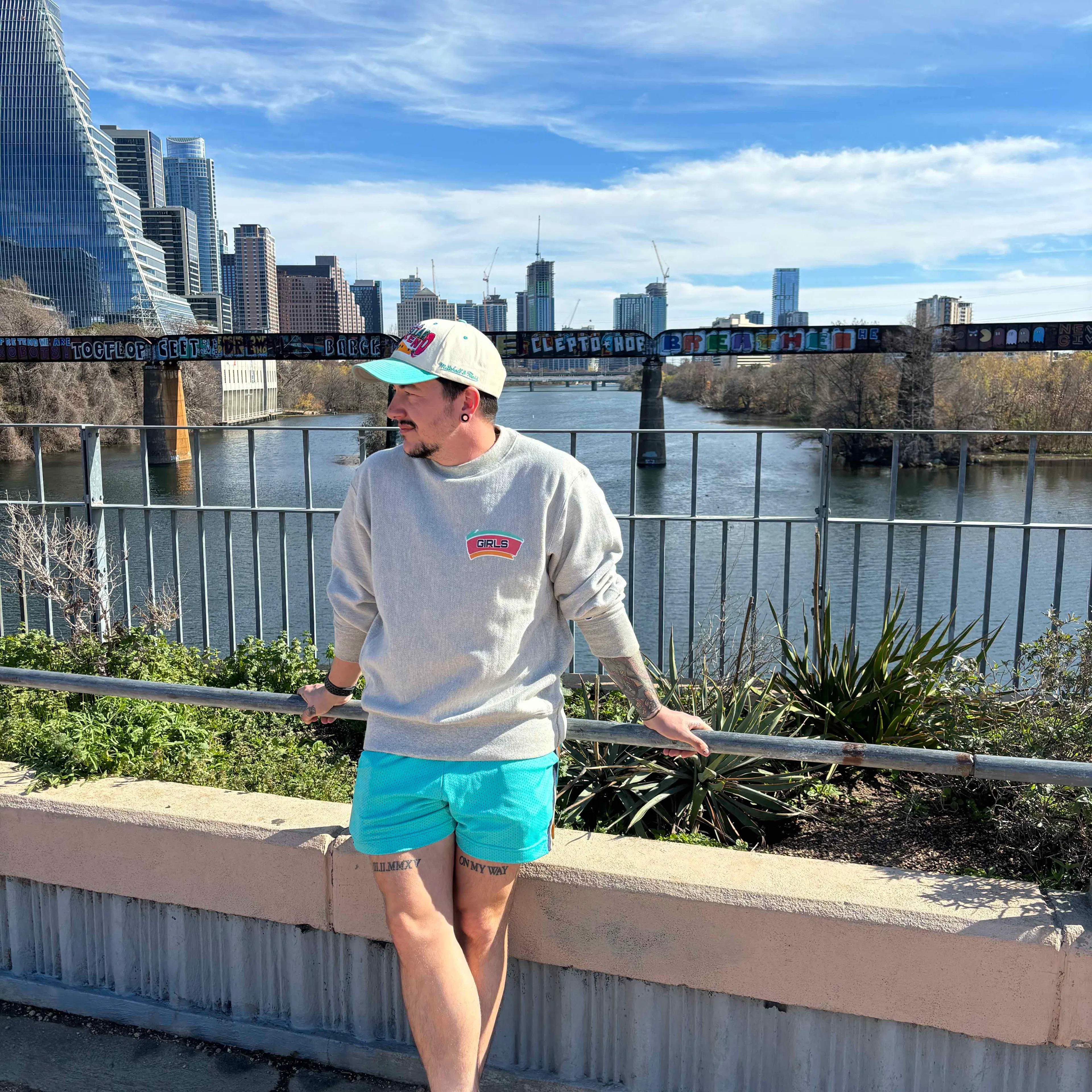 Chris Rhodes leaning on a railing by a river, with a city skyline behind