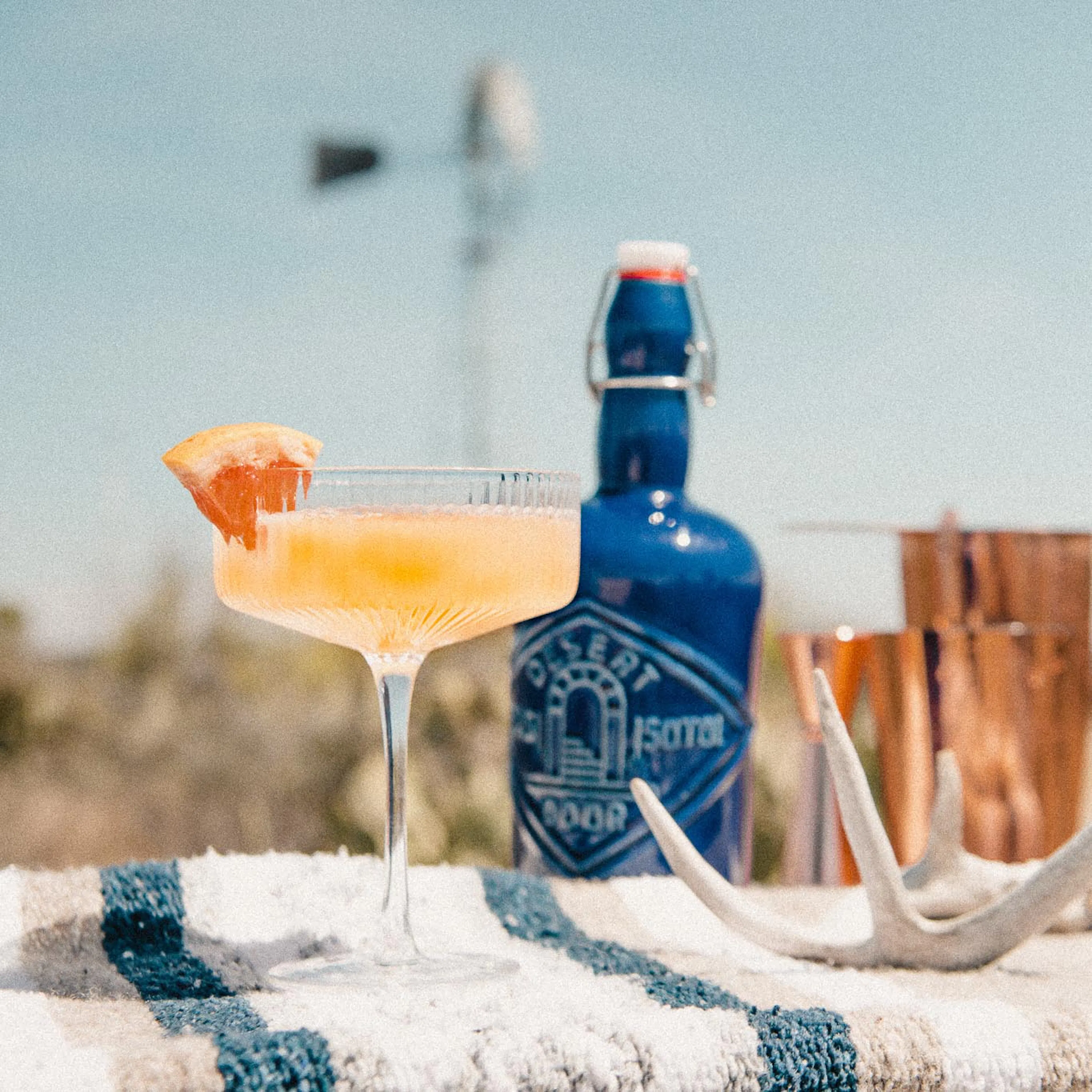 A cocktail with a grapefruit slice beside a blue Desert Door bottle