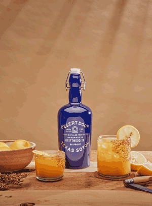 A blue Desert Door bottle beside cocktails garnished with lemon