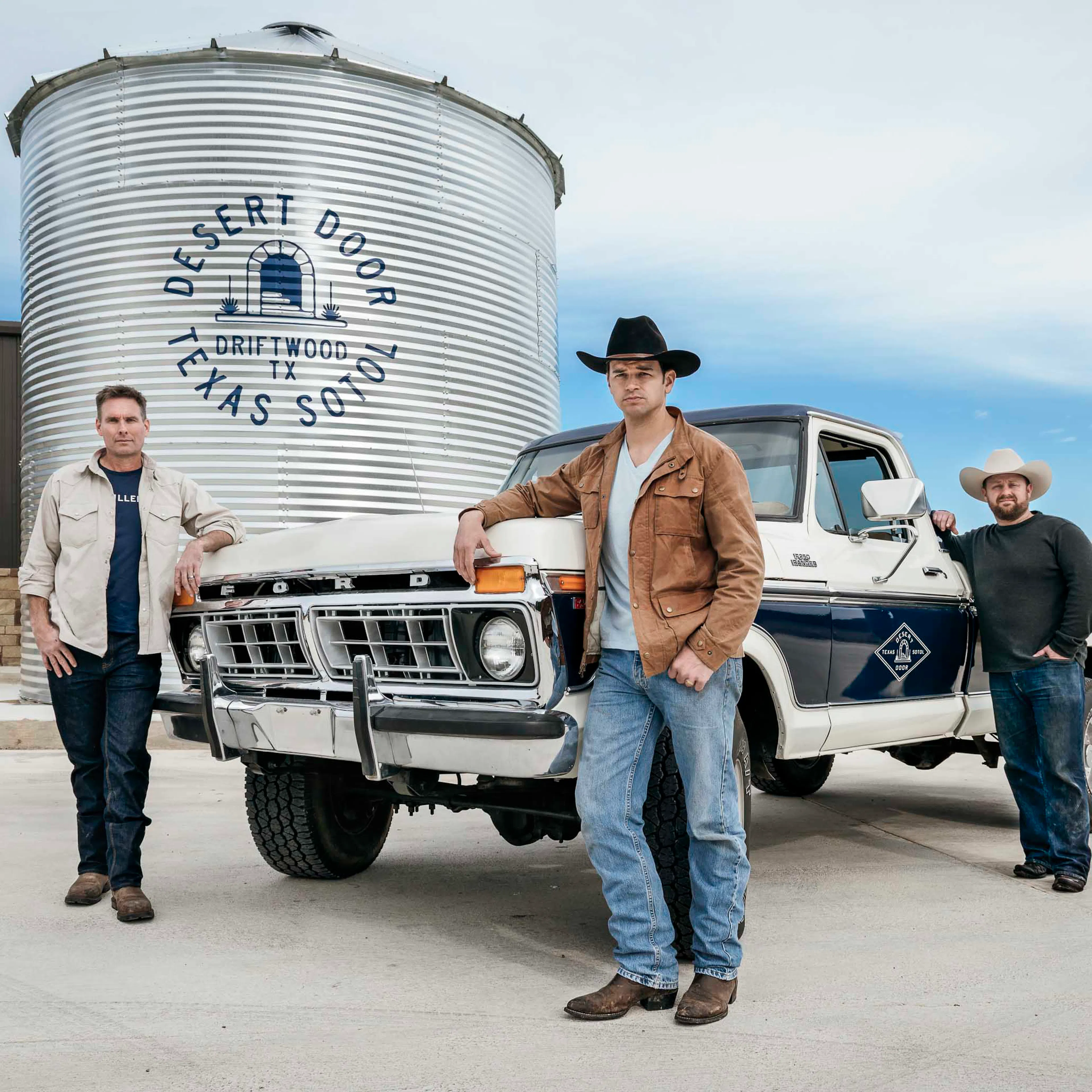 Three men in front of a Desert Door silo and a vintage pickup truck