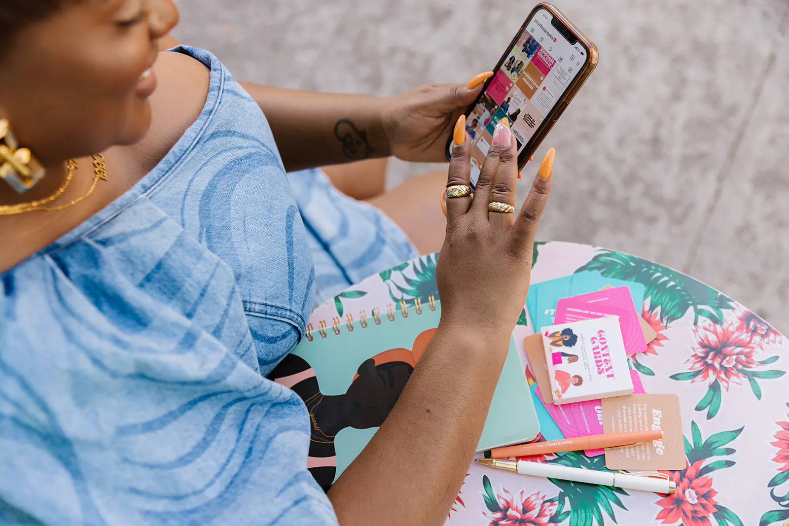 Hands scrolling a phone over a notebook and cards on a floral table