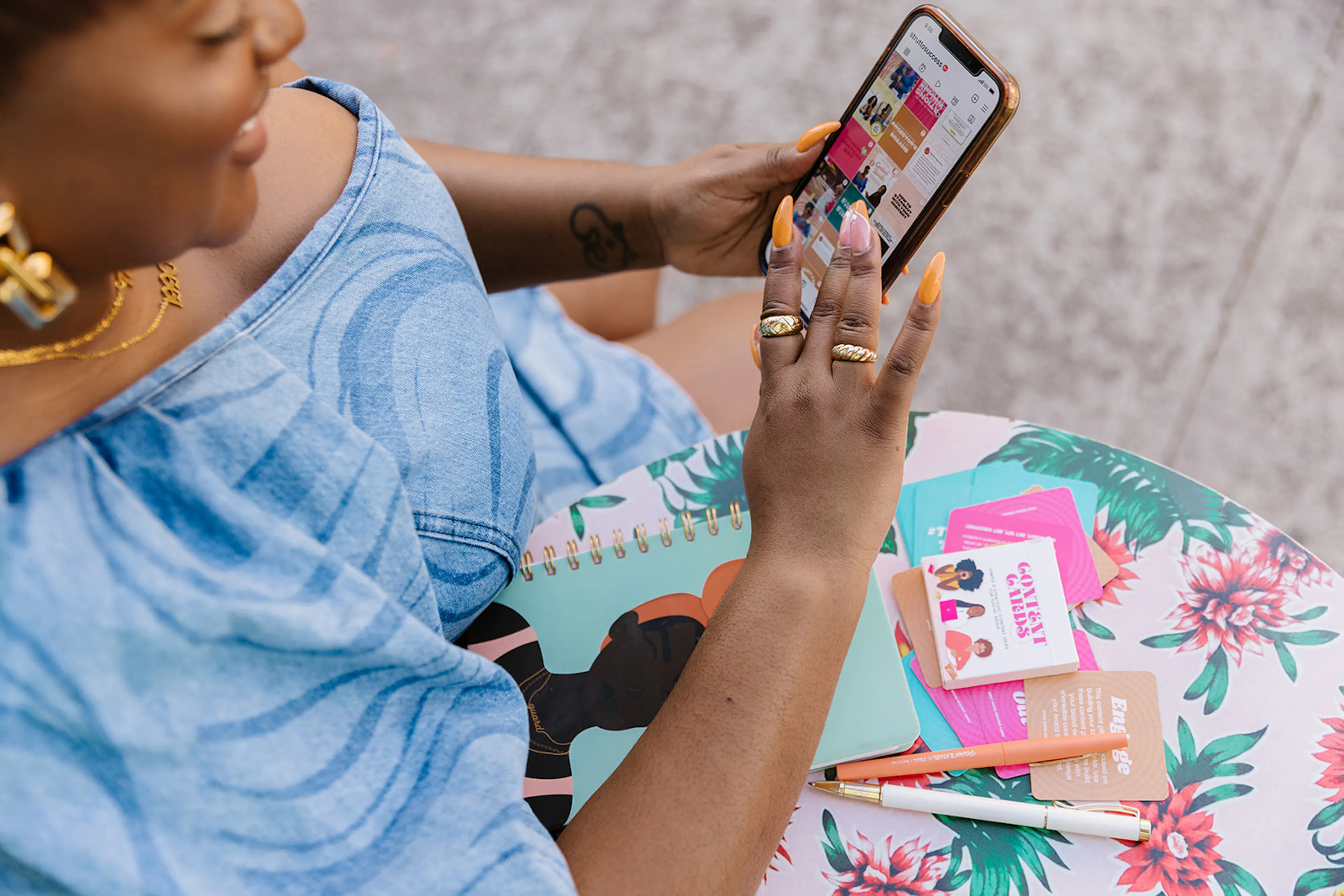 Hands scrolling a phone over a notebook and cards on a floral table