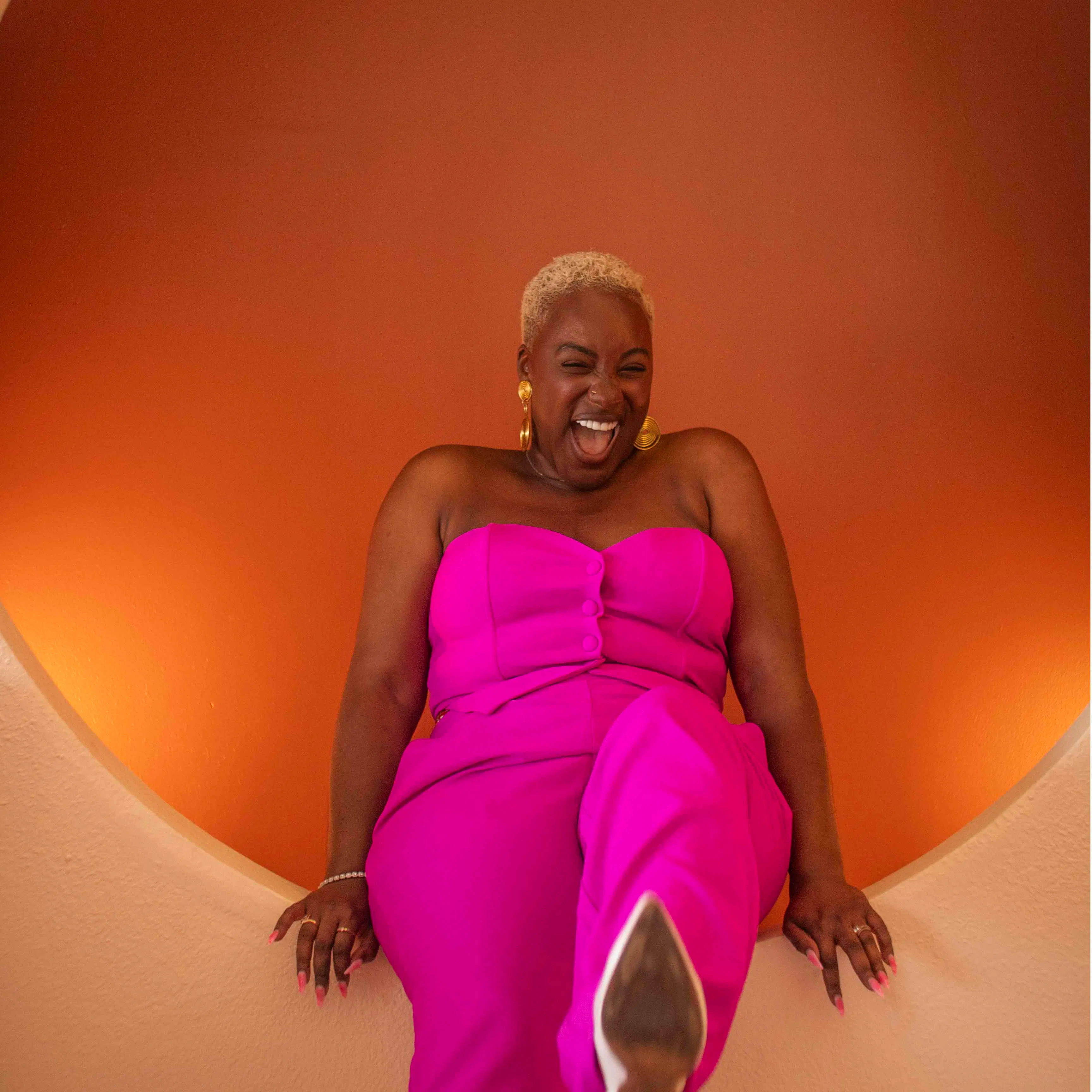 Gabriella Layne-Avery laughing in a pink outfit against an orange wall
