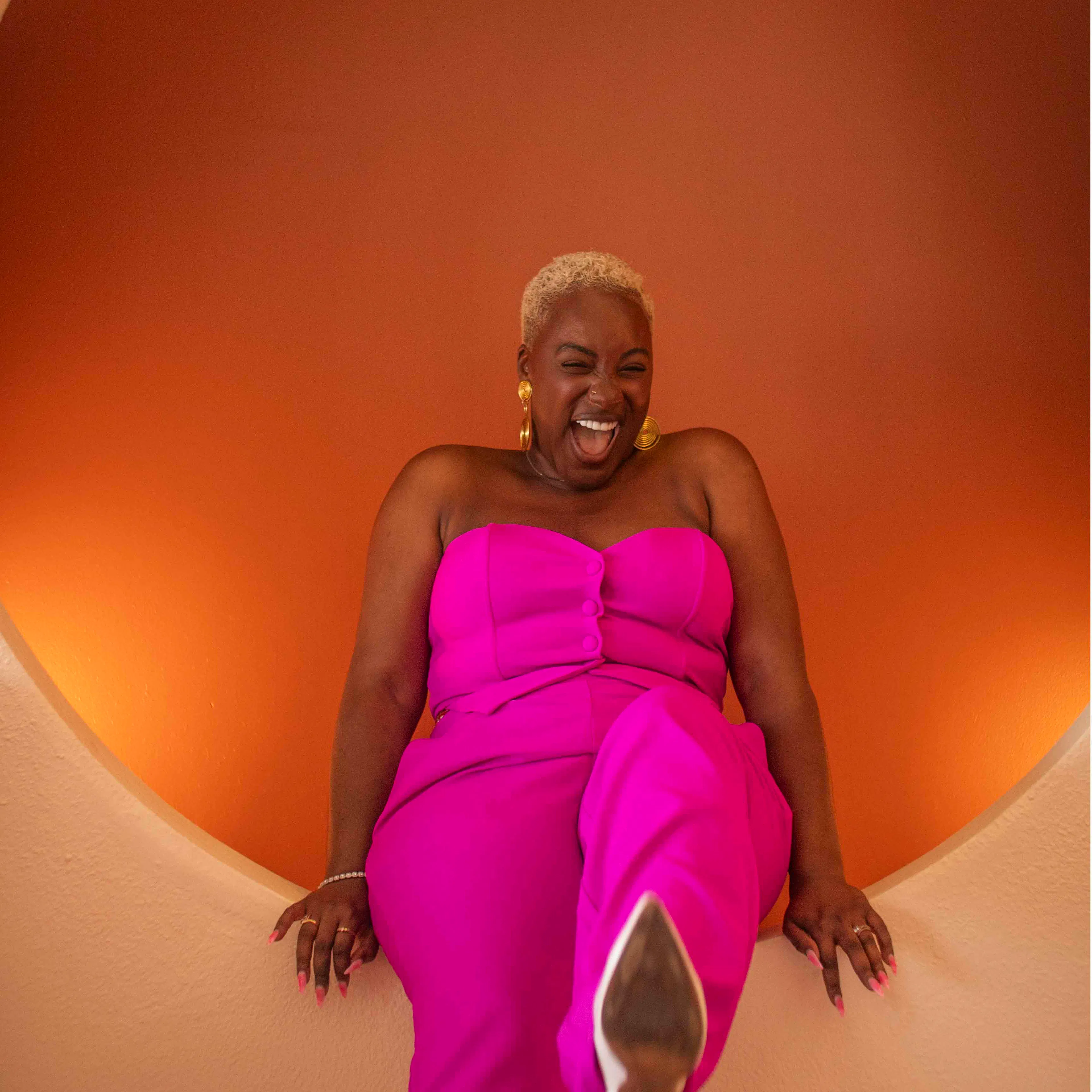 Gabriella Layne-Avery laughing in a pink outfit against an orange wall