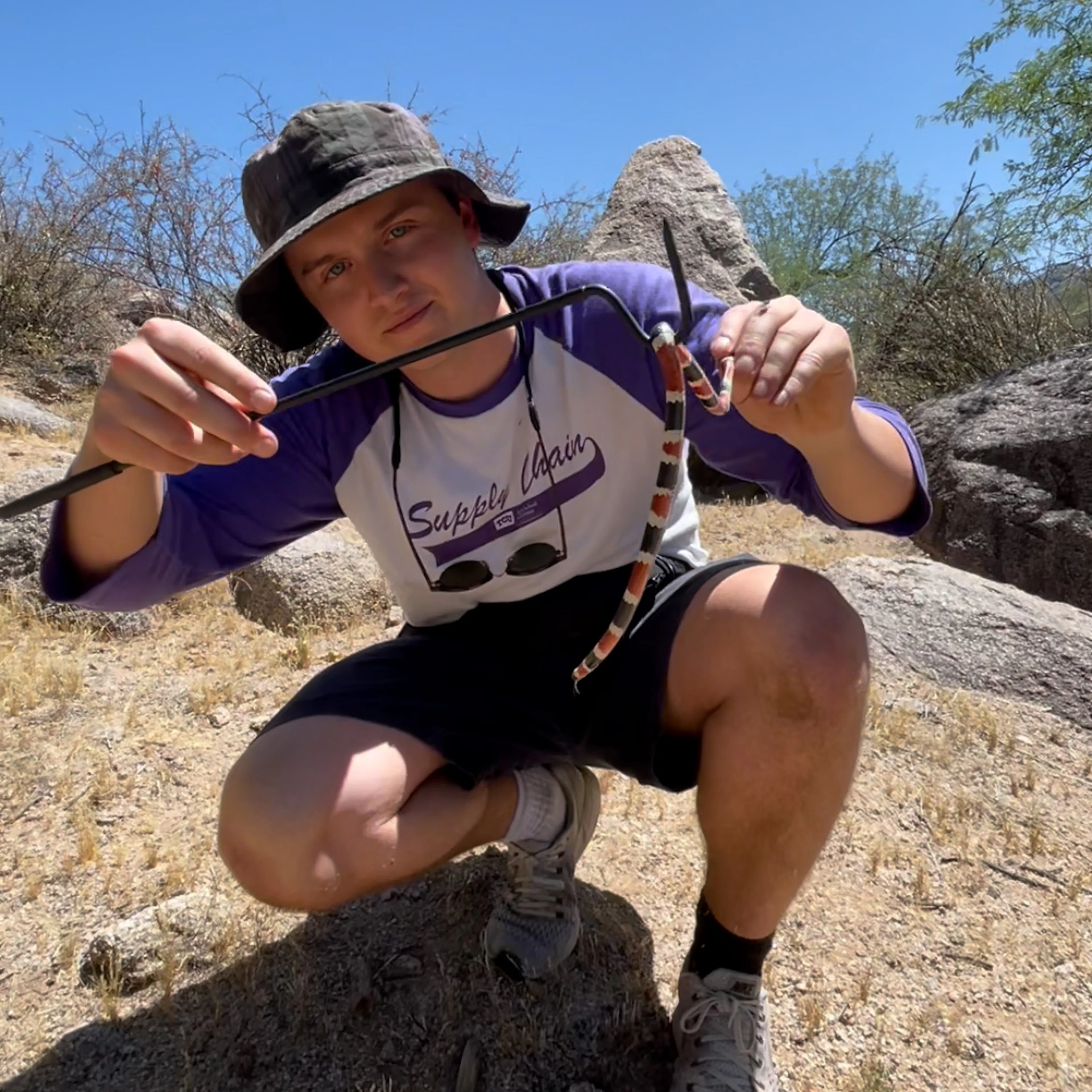 Jack Nailor crouching on a rock, holding a snake with a snake hook