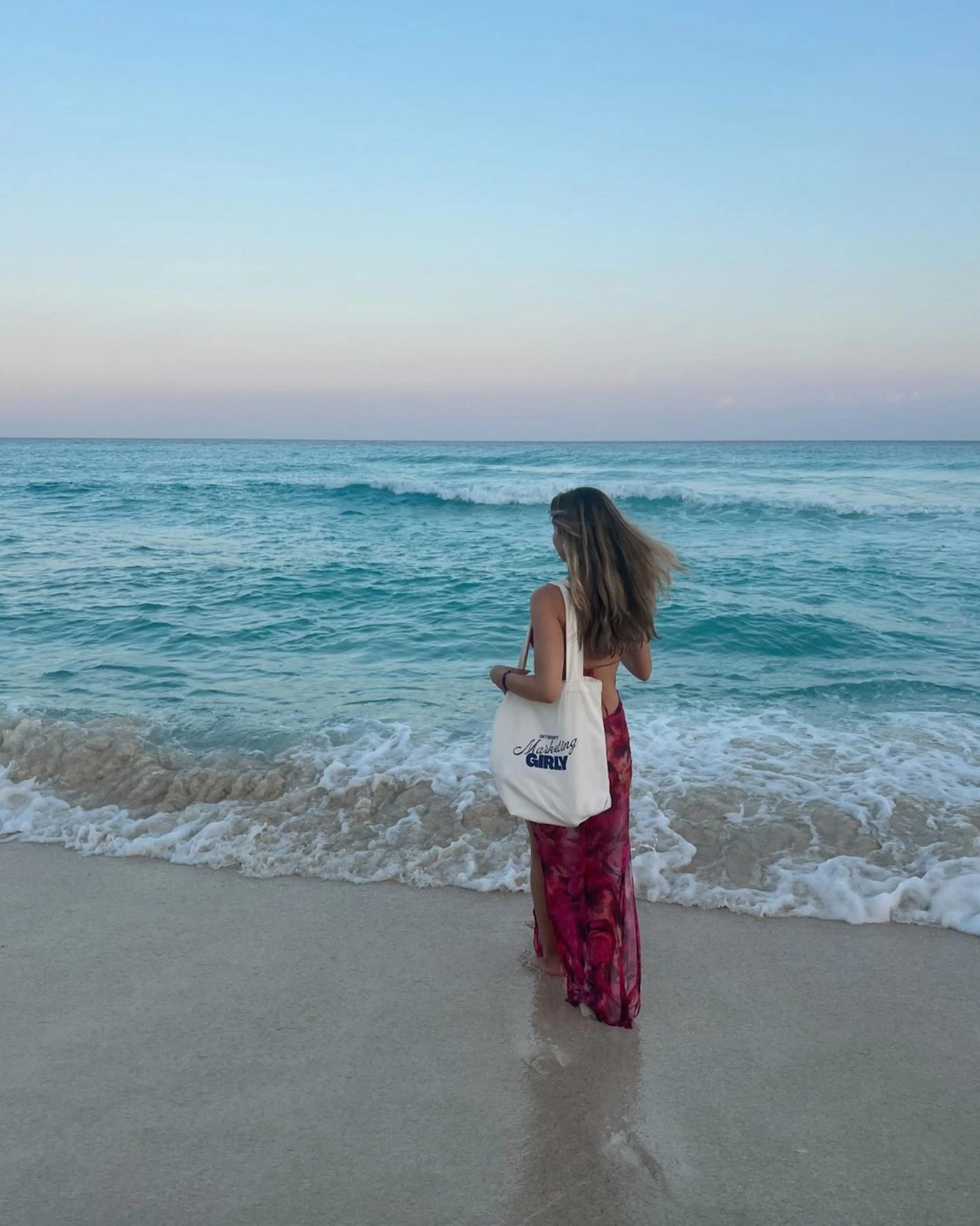 A woman standing at the water’s edge on a beach at sunset