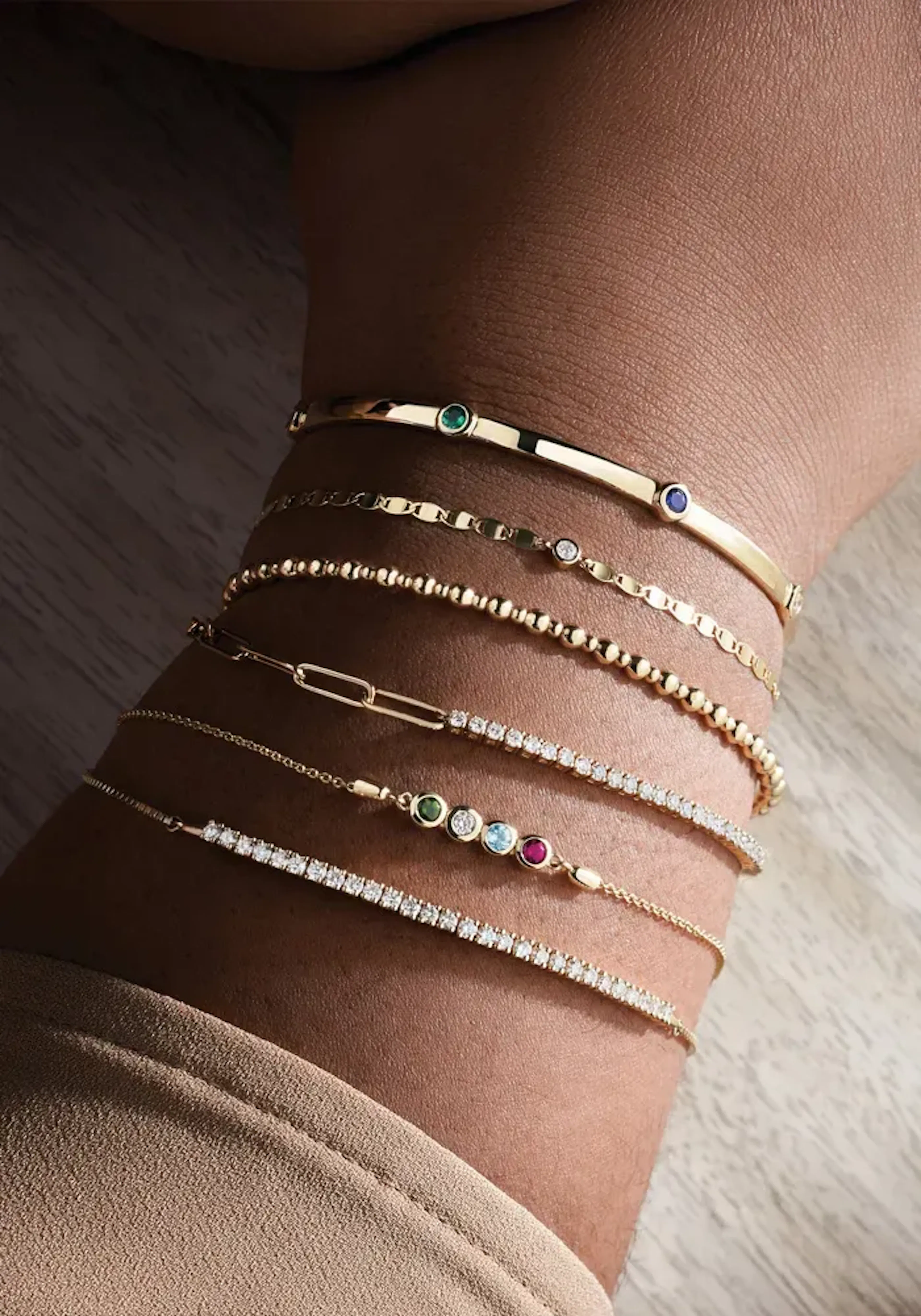 A stack of thin gold bracelets set with small stones on a wrist