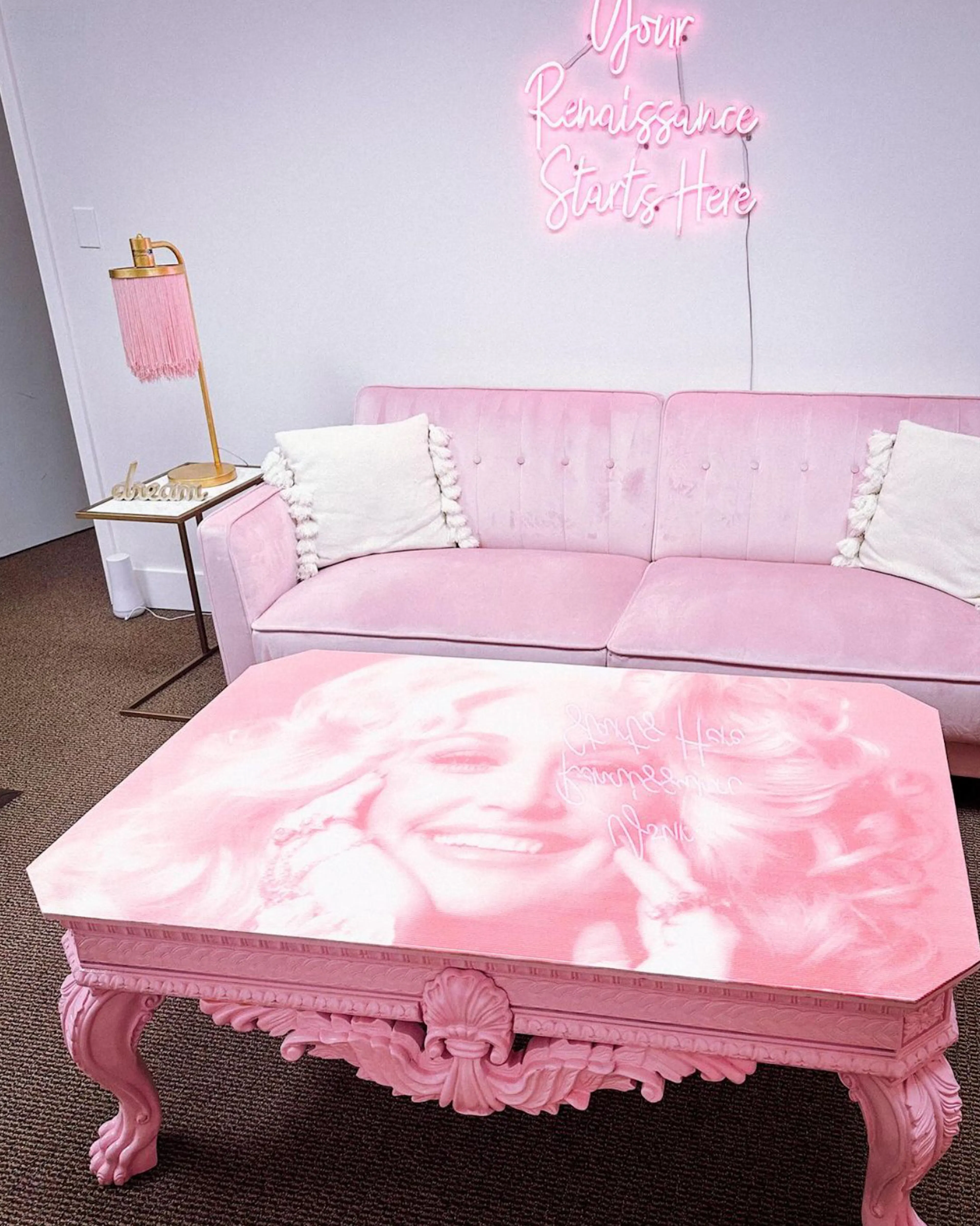 A pink studio with a velvet sofa under a “Your Renaissance Starts Here” neon sign