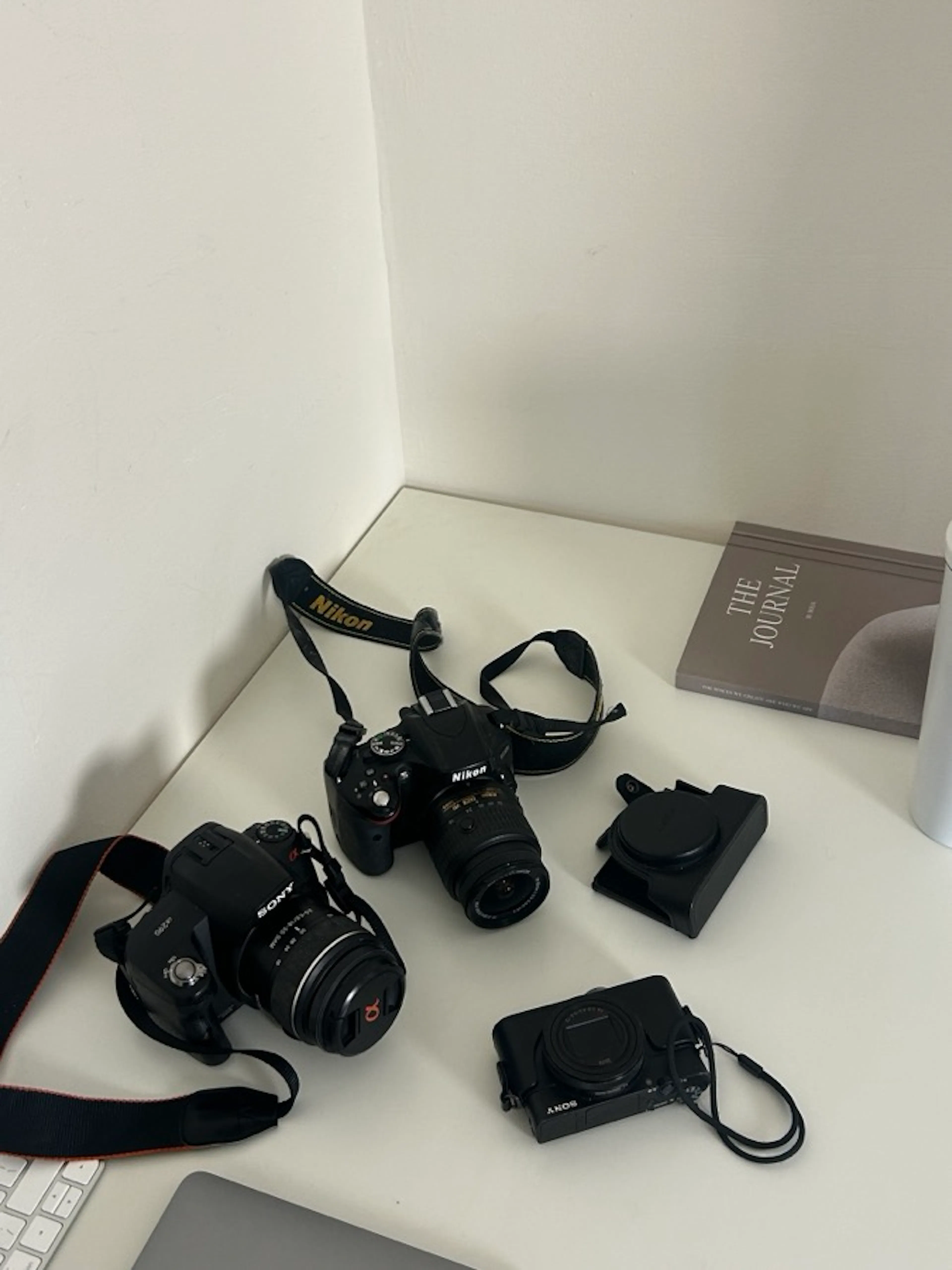 Four cameras and their straps on a white desk beside a journal.